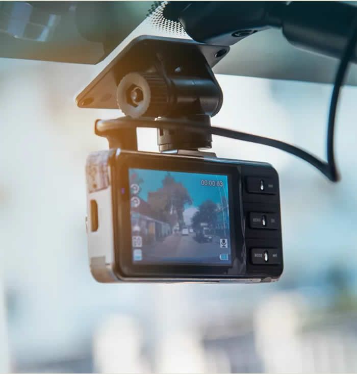 A vehicle video-tracking camera mounted to a windscreen, its rear screen showing the live forward view of the road it is recording.